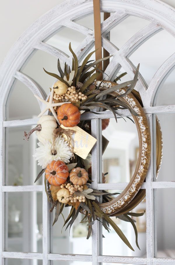A fall wreath with white and orange pumpkins made with a mirror frame.